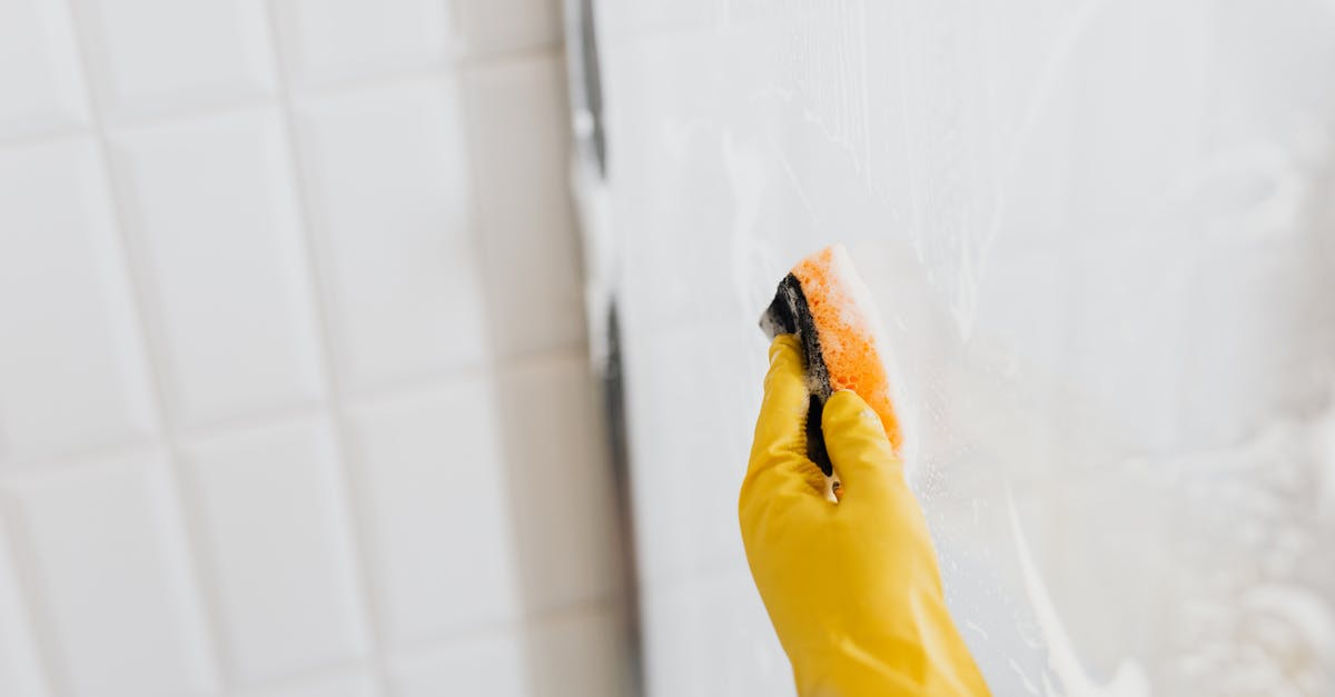 What does the maid mumble? - From above of crop anonymous person in yellow rubber protective glove washing shower cabin glass with sponge and detergent