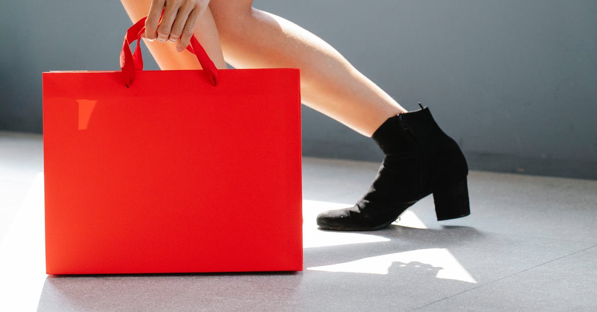 What evidence is there for each side of the debate over the authenticity of "Exit Through The Gift Shop"? - Side view of crop unrecognizable female in trendy boots holding red paper bag while standing on street on sunny day after shopping