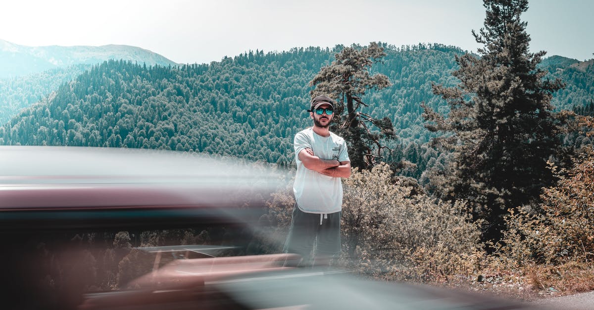 What exactly happened to the guys in Scenic Route movie? - Long exposure of male in casual clothing standing between mountains covered with woodland and car riding across road