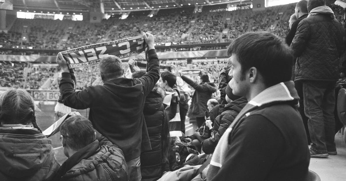 What happens to talk show giveaways that don't match the audience? - Black and white of group of people in warm clothing standing at stadium and watching match
