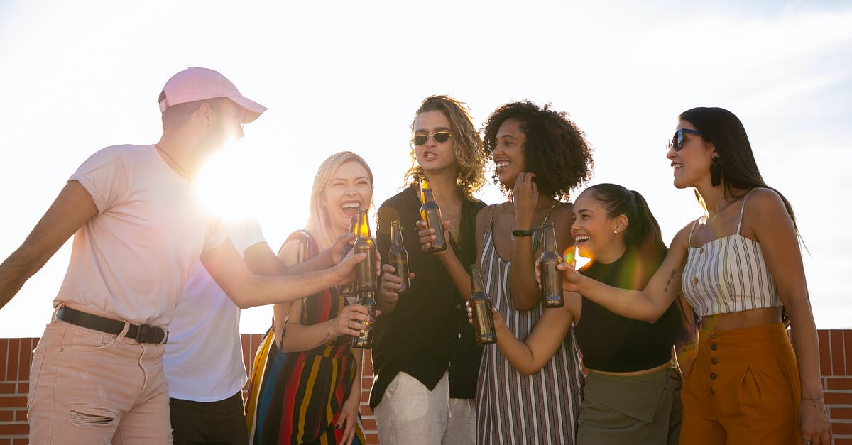 What is funny about "Can I have a chocolate donut and a bottle of beer"? - Group of joyful multiracial friends in summer outfits clinking beer bottles and laughing while gathering together on sunny rooftop