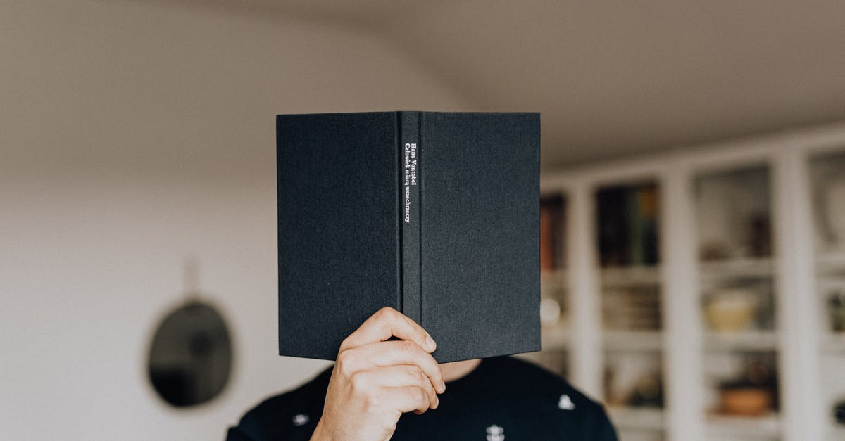 What is the difference between science fiction and horror? - Faceless male holding opened black book in hand covering face while standing in middle of light room