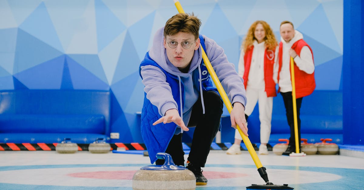 What is the point of throw the rock? - Concentrate male in sportswear with broom in hand throwing granite curling stone sliding on ice sheet while playing game near team