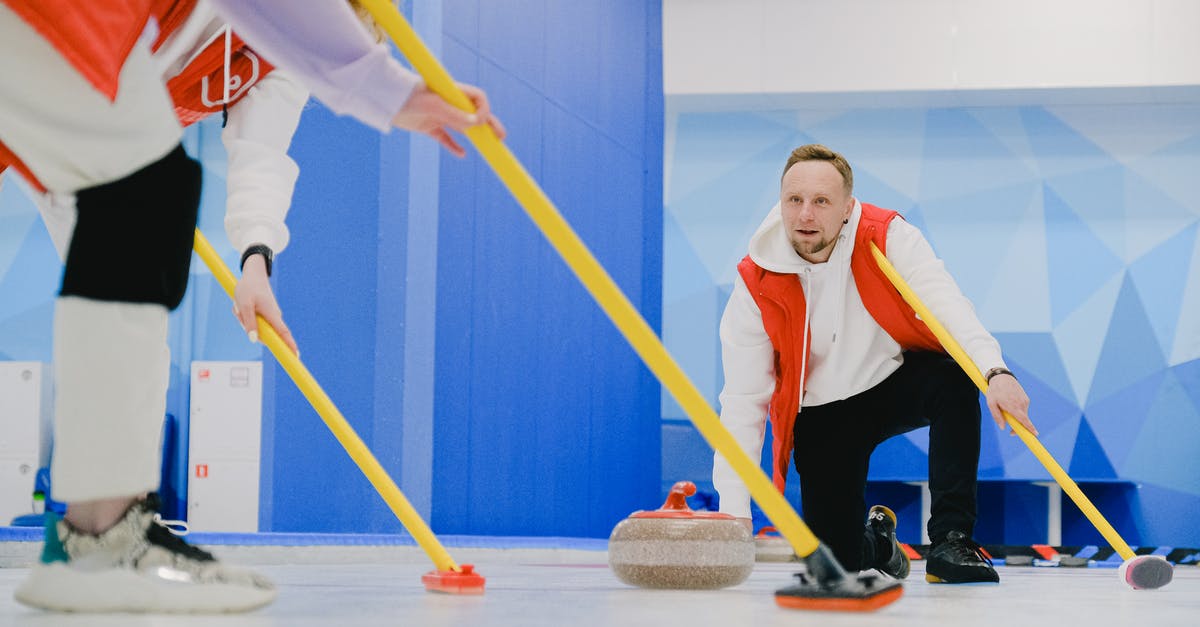 What is the point of throw the rock? - Determined sportsman throwing heavy granite curling stone near crop anonymous team sweeping ice sheet with brooms while playing sportive game
