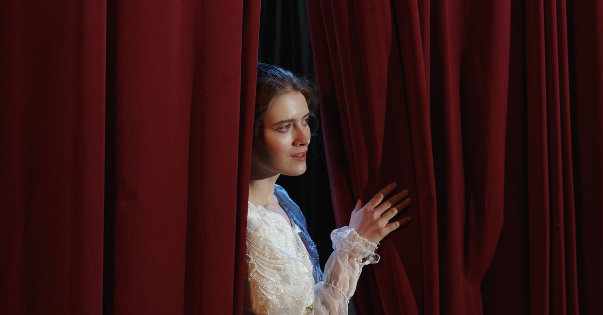 What is the reason behind the scenes played on TV in IT? - Woman in White Floral Lace Dress Standing Behind a Curtain