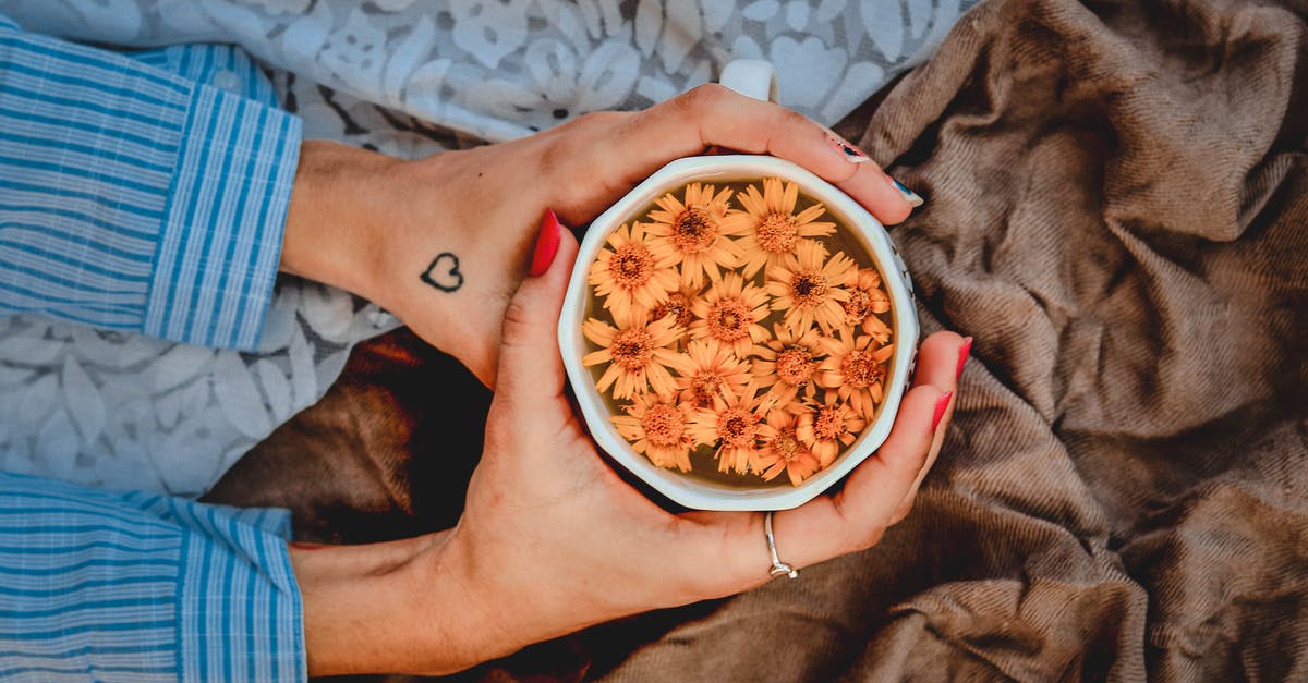 What is the significance of Shasta soft drinks? - Top view of crop anonymous female warming hands by ceramic mug with hot beverage decorated with fresh flowers