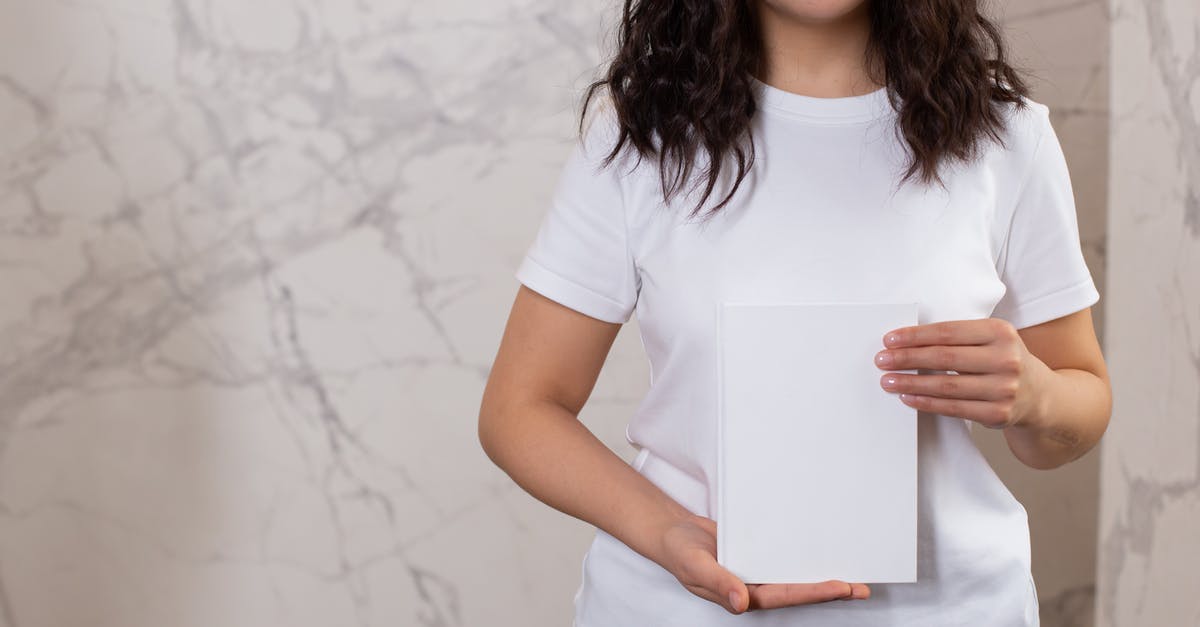 What is the significance of the book names' appearances? - Unrecognizable female with black hair and casual t shirt showing white black notepad while standing near wall in light room