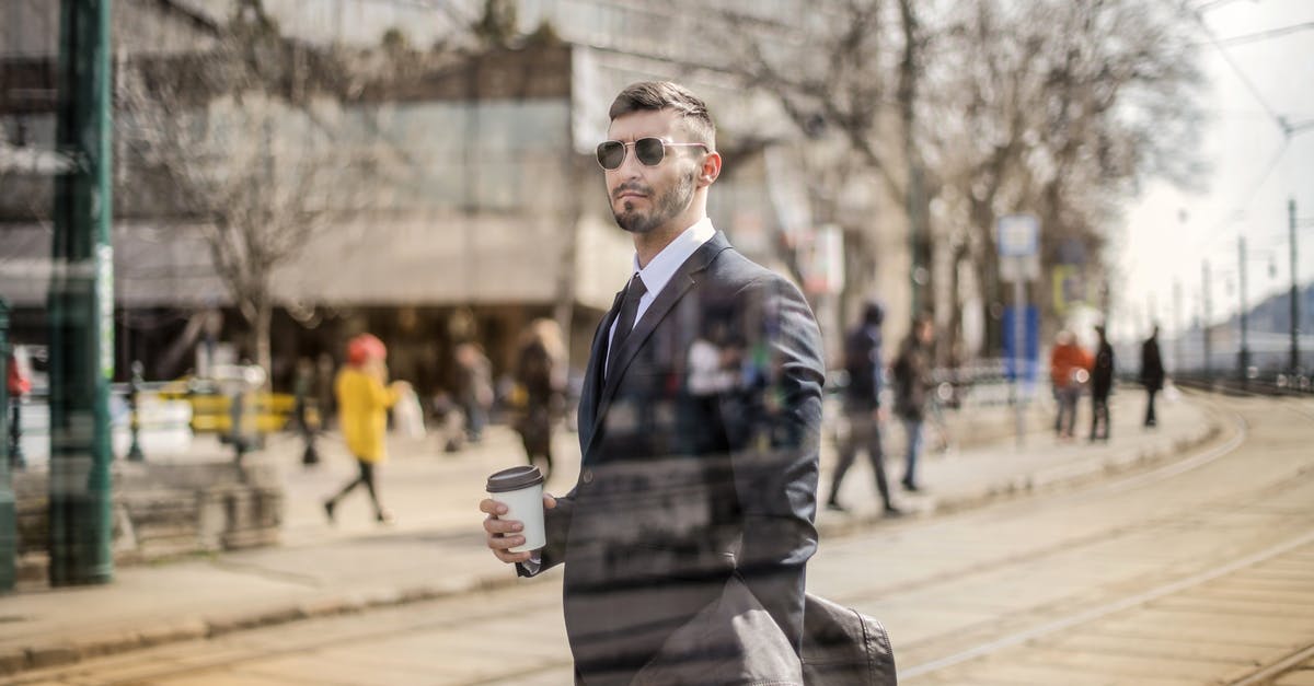 What is the Thai man saying to Maria as he drags her through the mud? - Through glass view of bearded man in suit and eyeglasses looking away while standing with coffee on city street
