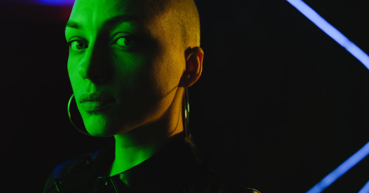 What is this shining look like effect called? - Crop unemotional bald female in black lather shirt looking at camera and standing in green neon light in darkness