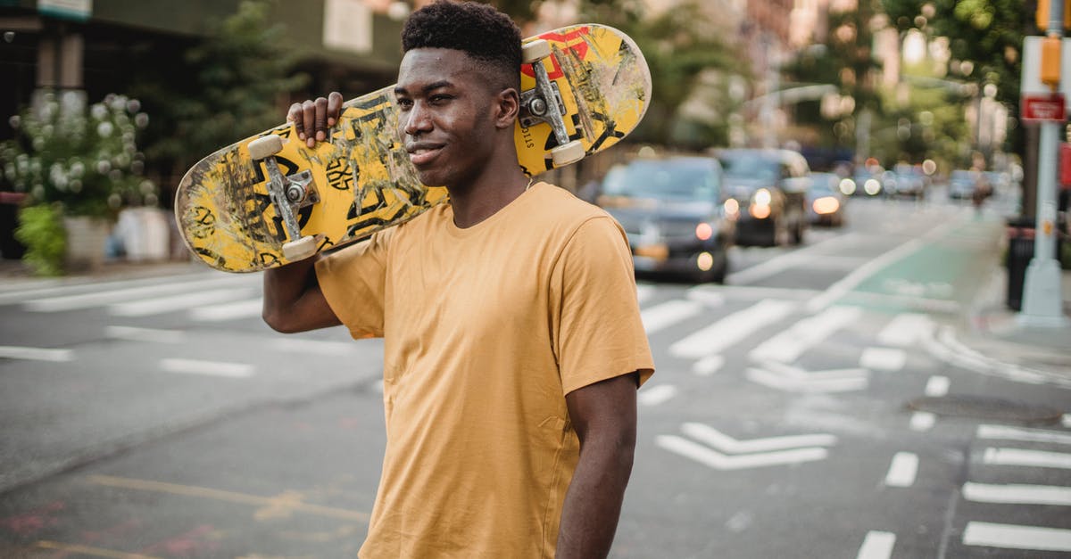 What motivated Mr. Smith to carry on? - Smiling fit African American male skater in casual shirt standing with skateboard on shoulder on urban street and looking away contentedly
