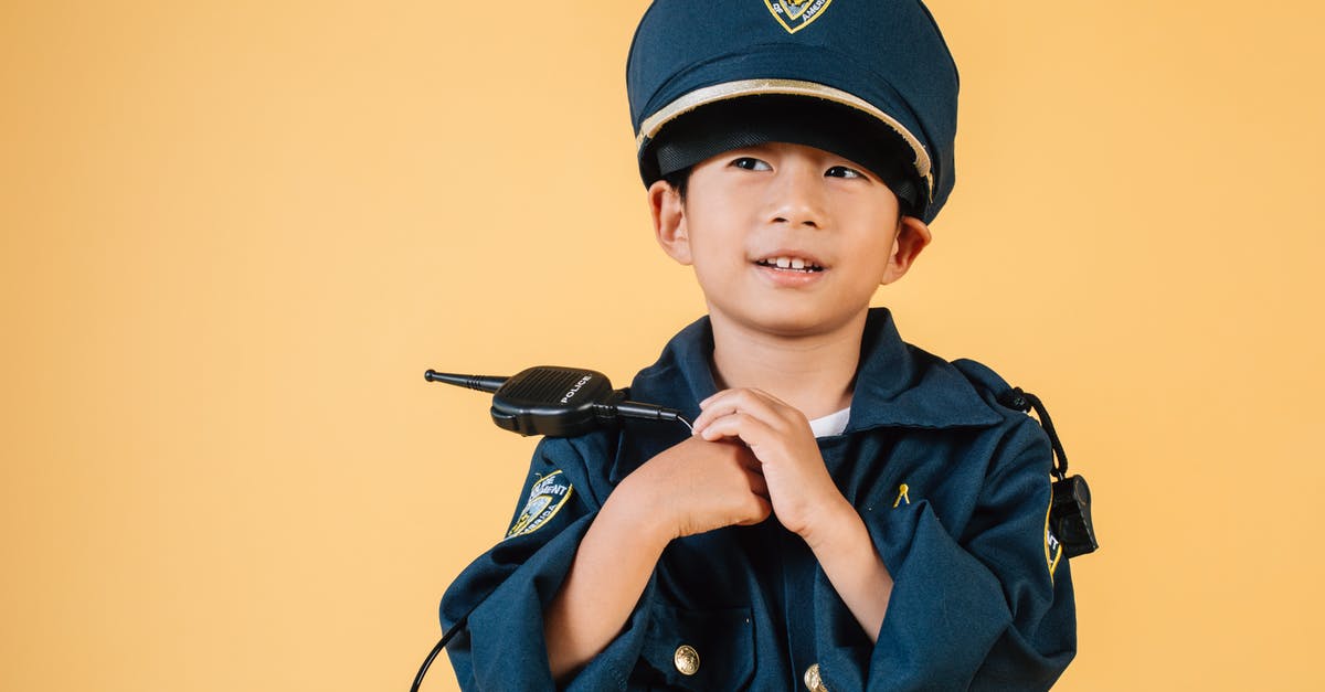 What purpose does the cop play in Hotel Artemis? - Pleasant Asian boy in police uniform and cap looking away while standing with hands near chest in studio on yellow background