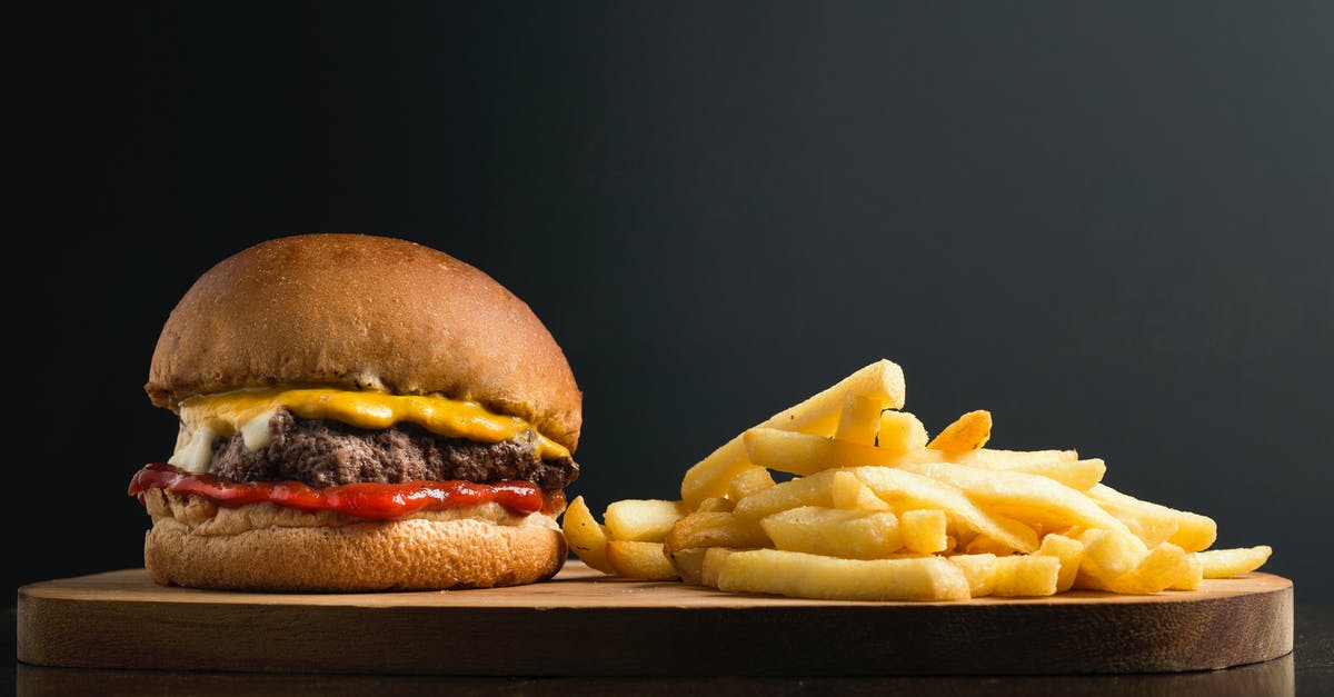 What questions is French referring to? - Appetizing burger with meat patty ketchup and cheese placed on wooden table with crispy french fries against black background