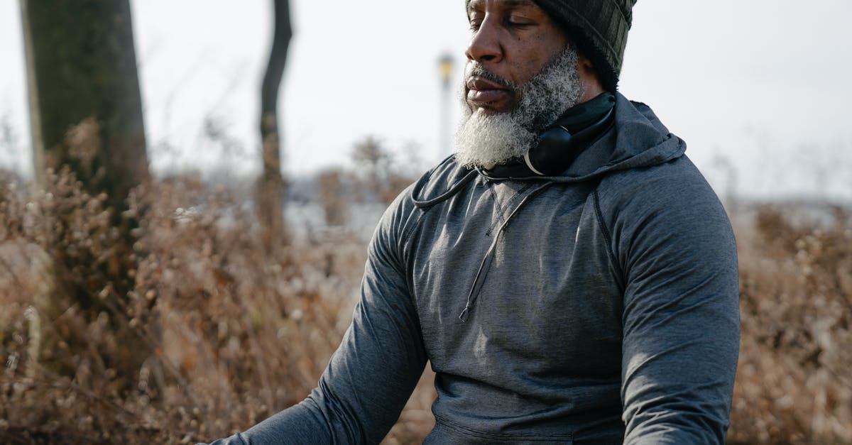 What trope would Indiana never leaving his hat behind fall under? - Bearded African American male in warm activewear and knitted hat sitting and meditating with closed eyes in autumn nature