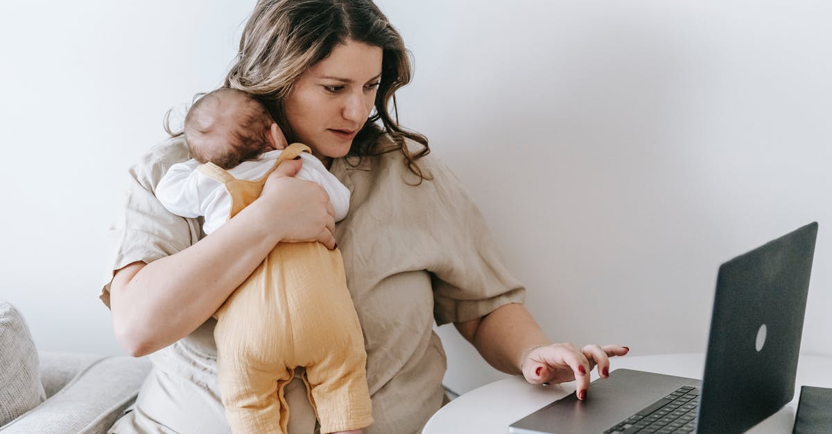 What type of creatures are the young ladies of Mrs. Poole? - Concentrated young female freelancer embracing newborn while sitting at table and working remotely on laptop at home