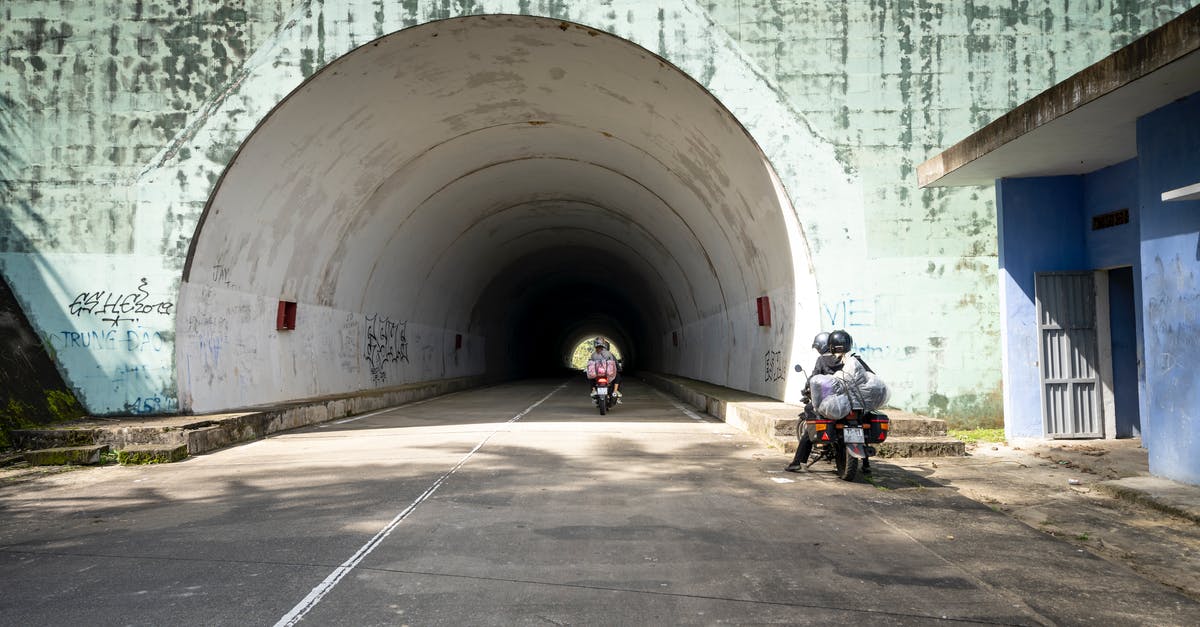 What was the meaning of the tunnel scene? - People riding motorbikes on straight asphalt roadway leading to shabby tunnel near old building in suburb area of sunny countryside