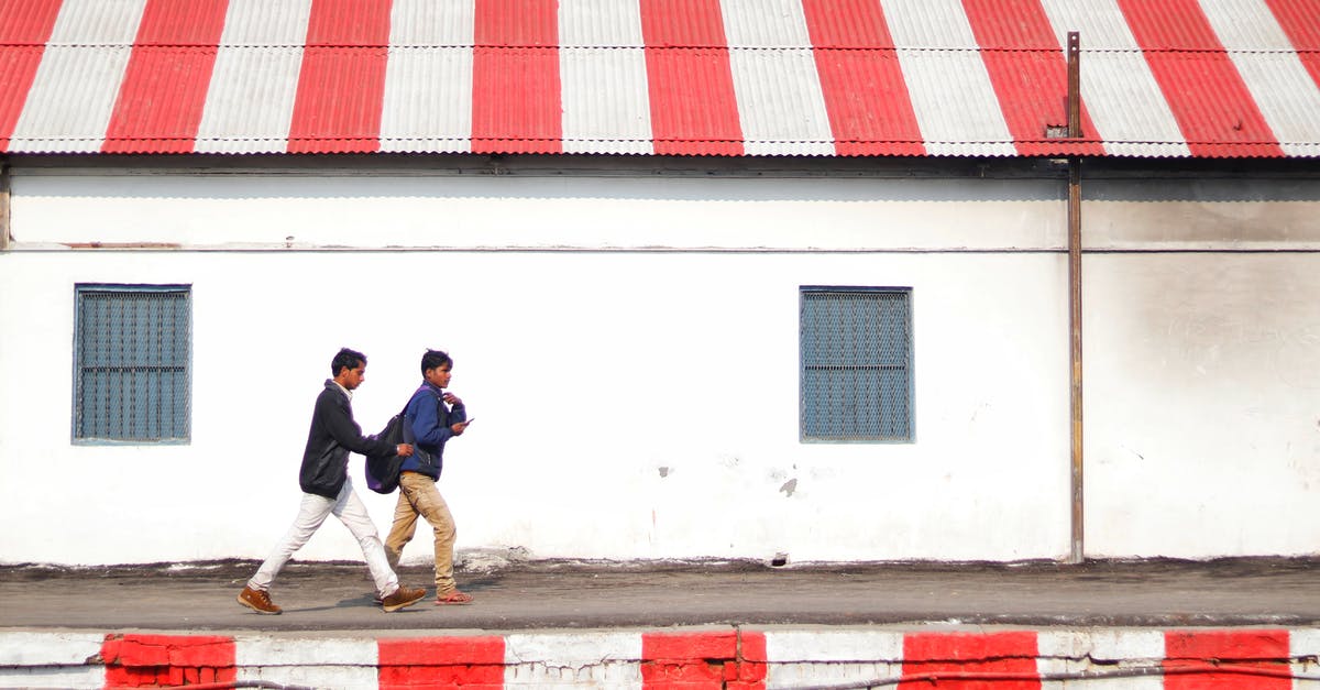 What was the significance of Red Indian and the Mascot's appearances? - Side view of young Asian guys walking on platform painted with white and red stripes along shabby stone building with striped white and red roof on daytime
