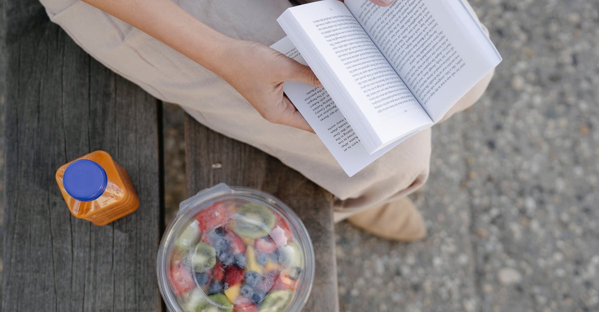 Where did the box go? - From above of crop unrecognizable female reading textbook on street bench with refreshing drink and fruit salad in takeaway container