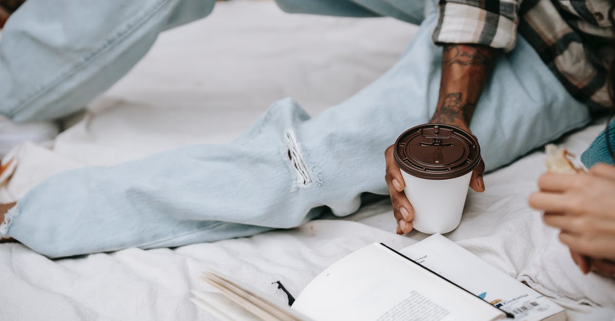 Where did the leg go? - Crop unrecognizable ethnic person in jeans and checkered shirt lying on blanket with cup of coffee and book
