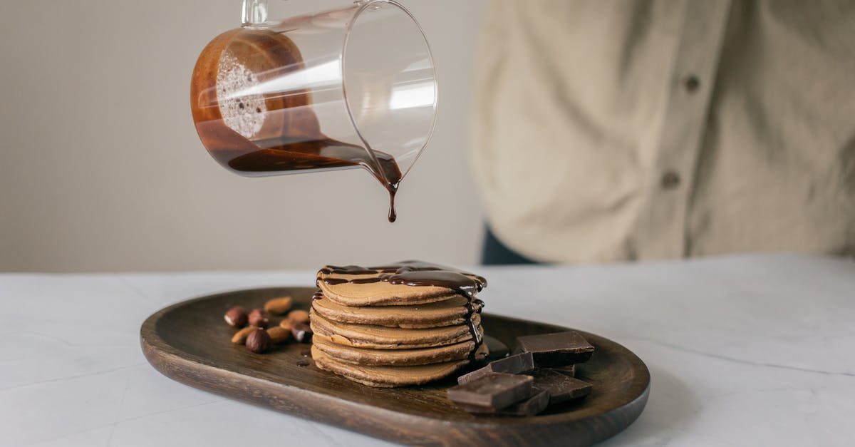 Which came first - Chef's Chocolate Salty, or Schweddy Balls? - Crop anonymous person pouring fresh chocolate from jug on appetizing pancakes placed on timber board on table