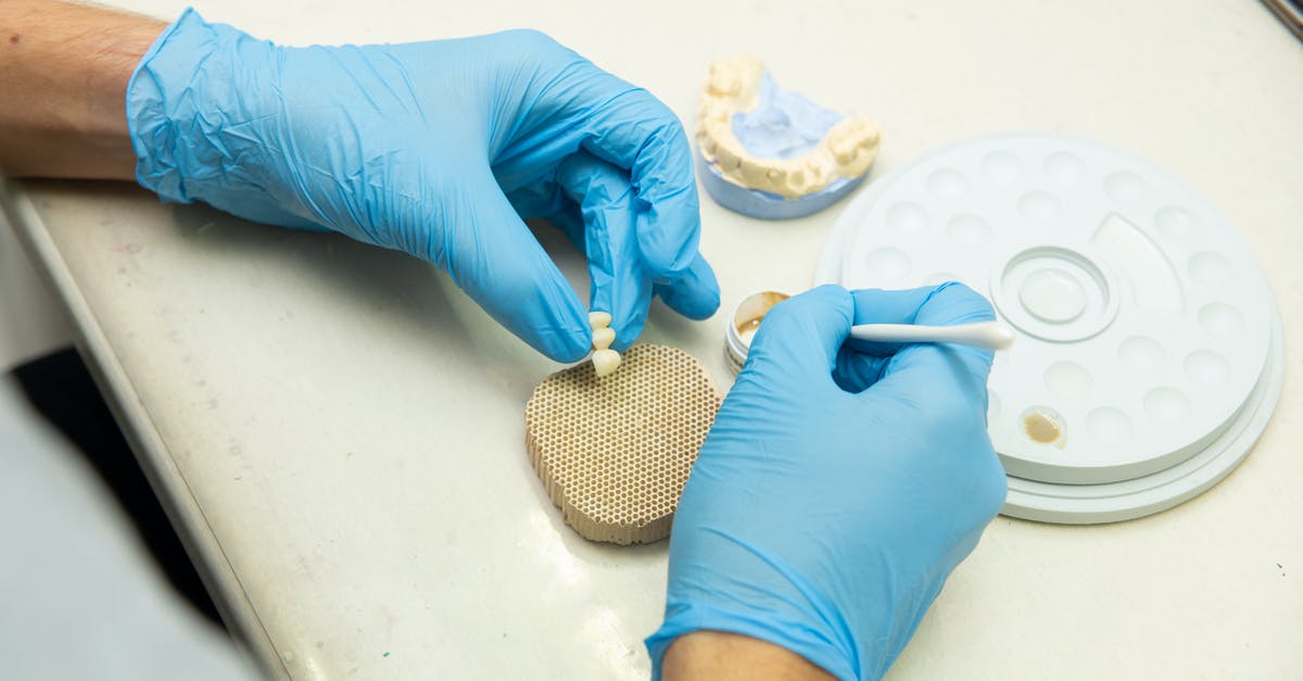 Which material are fake eyeballs made off? - From above of crop anonymous orthodontist in latex gloves creating fake teeth for denture while sitting at table in light dental clinic