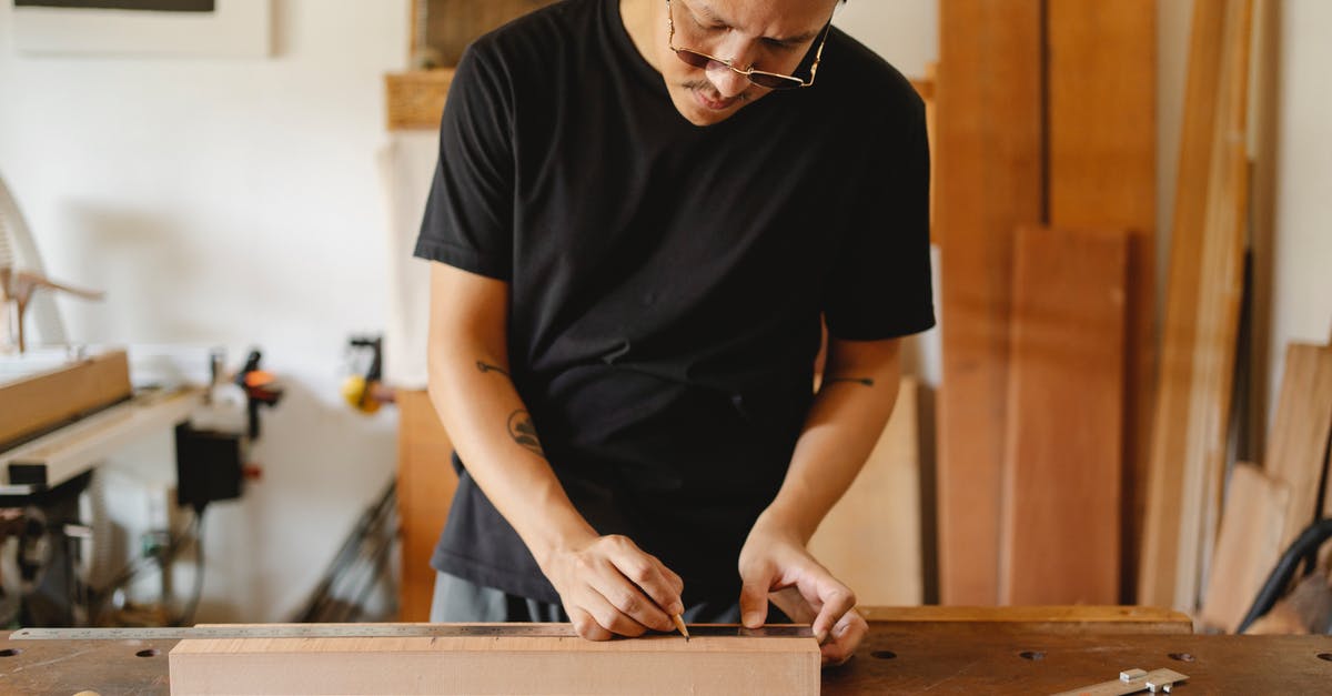 Who's in on the master plan? - Crop serious ethnic male making marks on timber plank and working on wooden table in carpentry shop