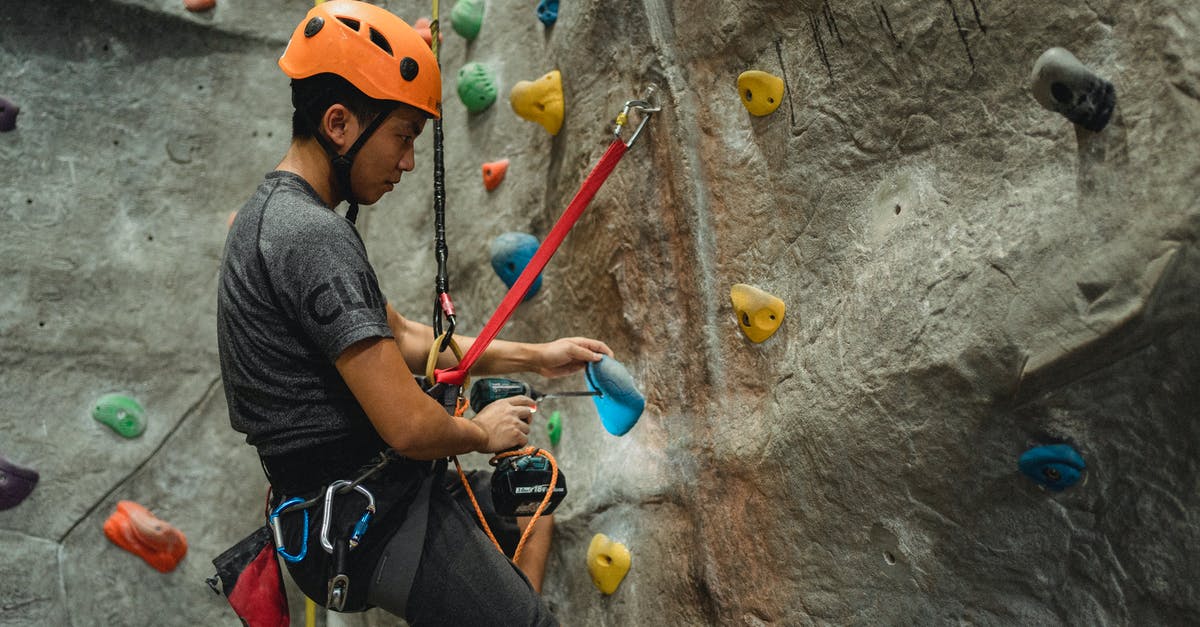Who's Tom Bishop's support in China? Is it the same guy he worked with in 'Nam? - From below of side view of Asian male specialist in helmet drilling hole in blue climbing hold while hanging on safety rope near bouldering wall