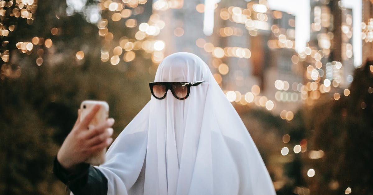 Who are the people who mug the ghost outside of Rhinehart's publishing firm? - Anonymous person wearing ghost costume and sunglasses taking self portrait on smartphone while standing on street with trees and skyscrapers on blurred background during Halloween