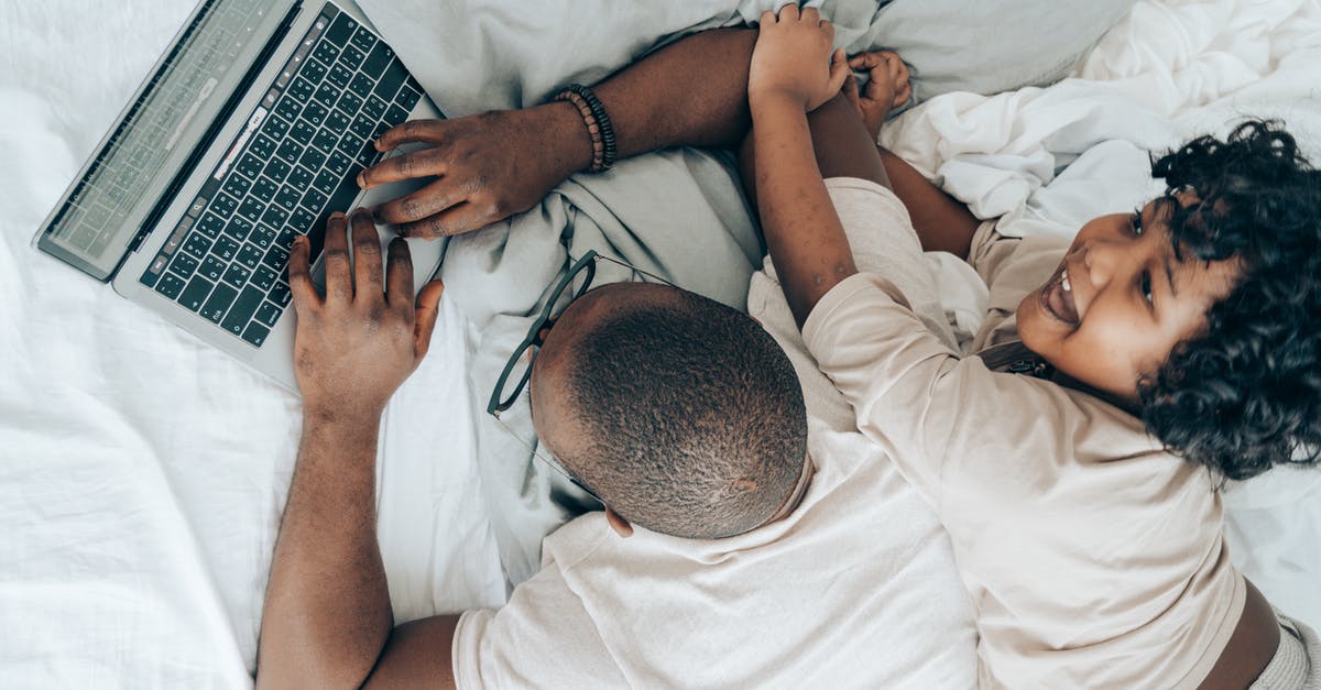 Who kills T'Chaka, one of the original Black Panthers + father of the current Black Panther? - Top view of cheerful African American kid lying near father while man typing on keyboard of laptop during remote work in cozy bedroom
