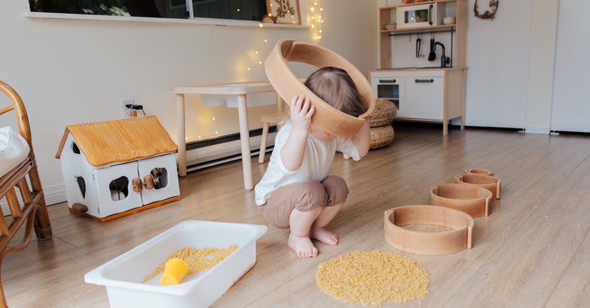 Who put the Hangman game on the refrigerator? - Full length of anonymous toddler squatting barefoot on floor playing with round wooden shapes of different size and pasta and putting biggest shape on while developing fine motor skills at home
