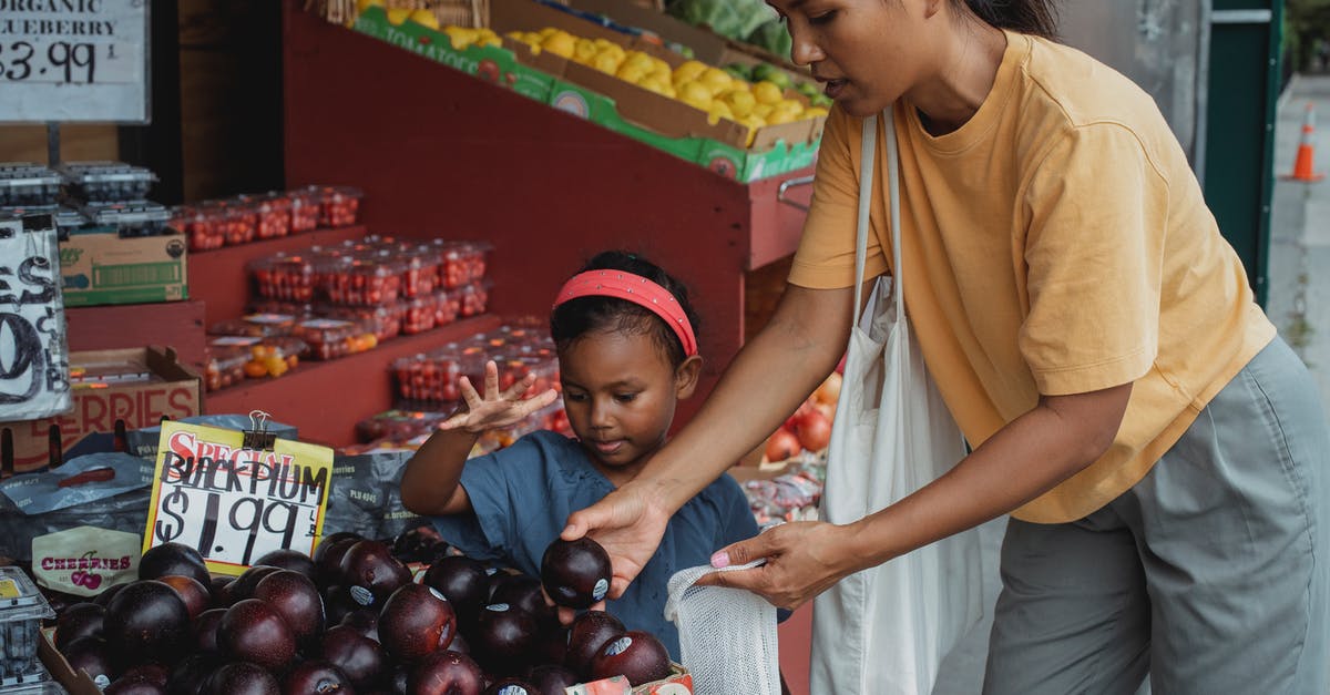 Who put the key in the box, and how did they get it? - Asian woman putting black plum into eco bag while choosing fruits from box in street market with daughter