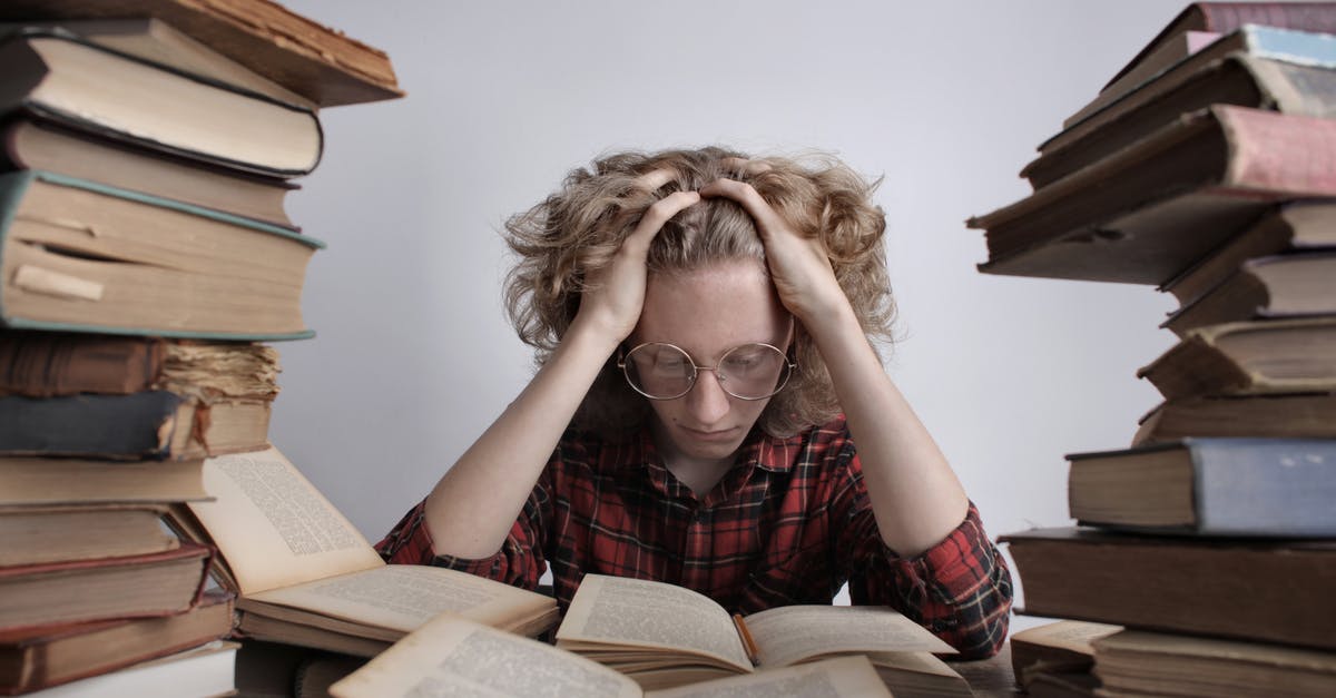 Who recruited this many students without informing Bartleyby? - Tired teenage boy in casual clothes and eyeglasses sitting at desk with large stacks of books holding head and reading book while preparing for exam