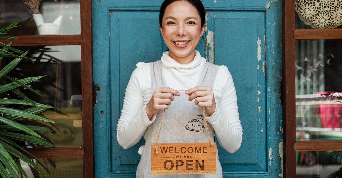 Who showed content warnings (you know after ratings bumpers) first, HBO or Cinemax? - Cheerful ethnic female cafeteria owner in apron demonstrating cardboard signboard while standing near blue shabby door and windows after starting own business and looking at camera