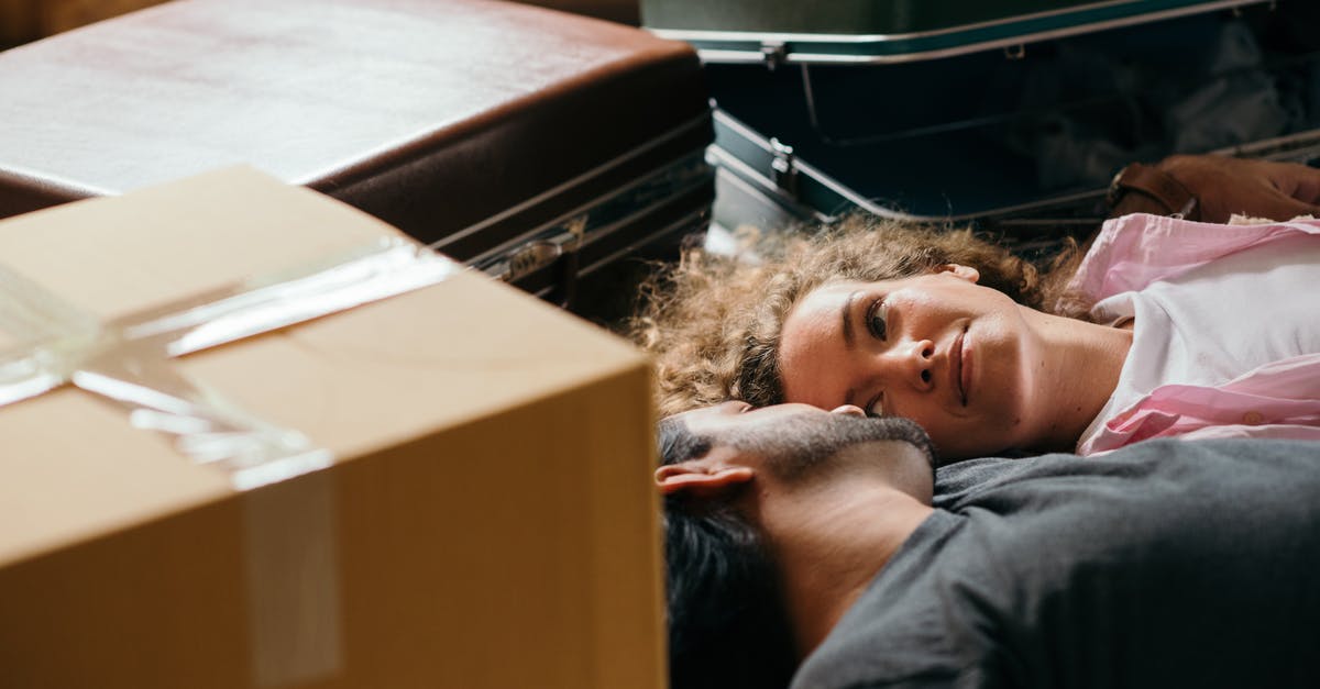 Who threw the suitcase to the other? - From above of man and woman looking at each other while lying on floor during preparing for relocation among carton boxes and suitcases