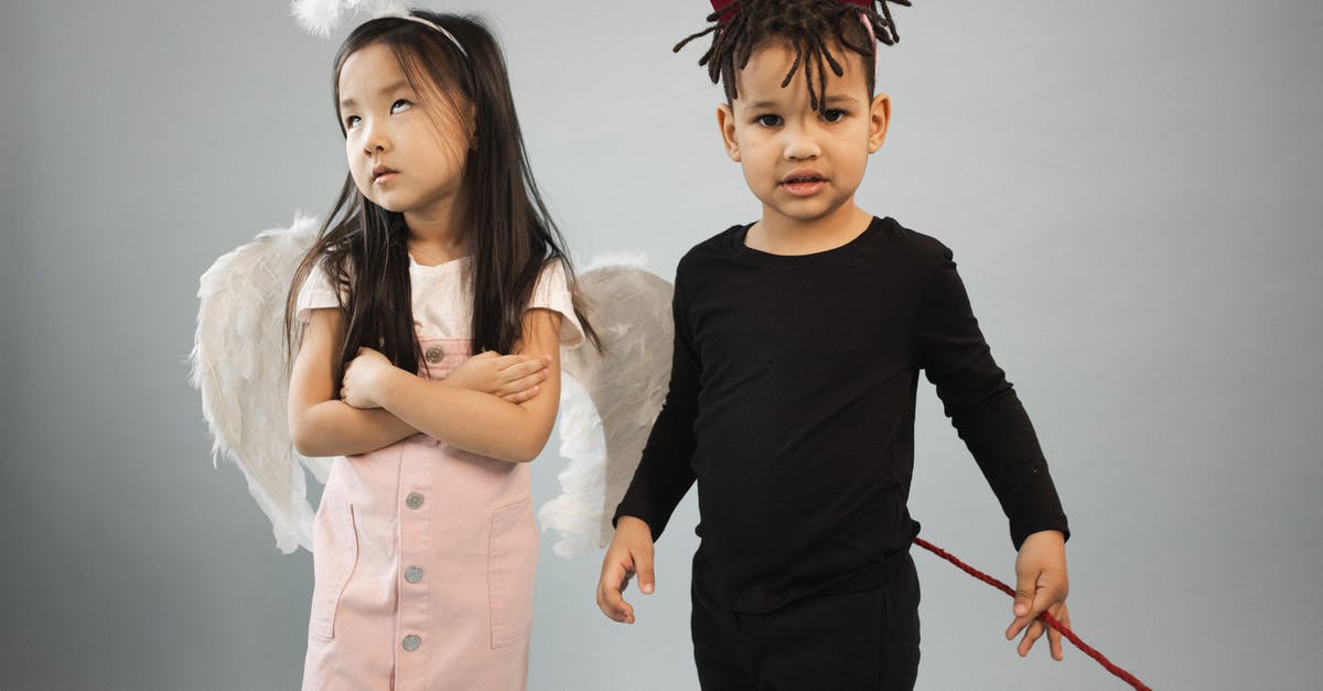 Who was Angel Eyes trying to shoot first? - Adorable Asian girl in angel costume with halo standing near black boy in devil outfit looking at camera on gray background in studio