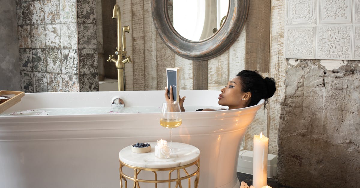 Who was the old lady in the woods? - Side view of young African American female reading book while lying in bathtub and enjoying spa procedure with wine glass on small marble table and aroma candles