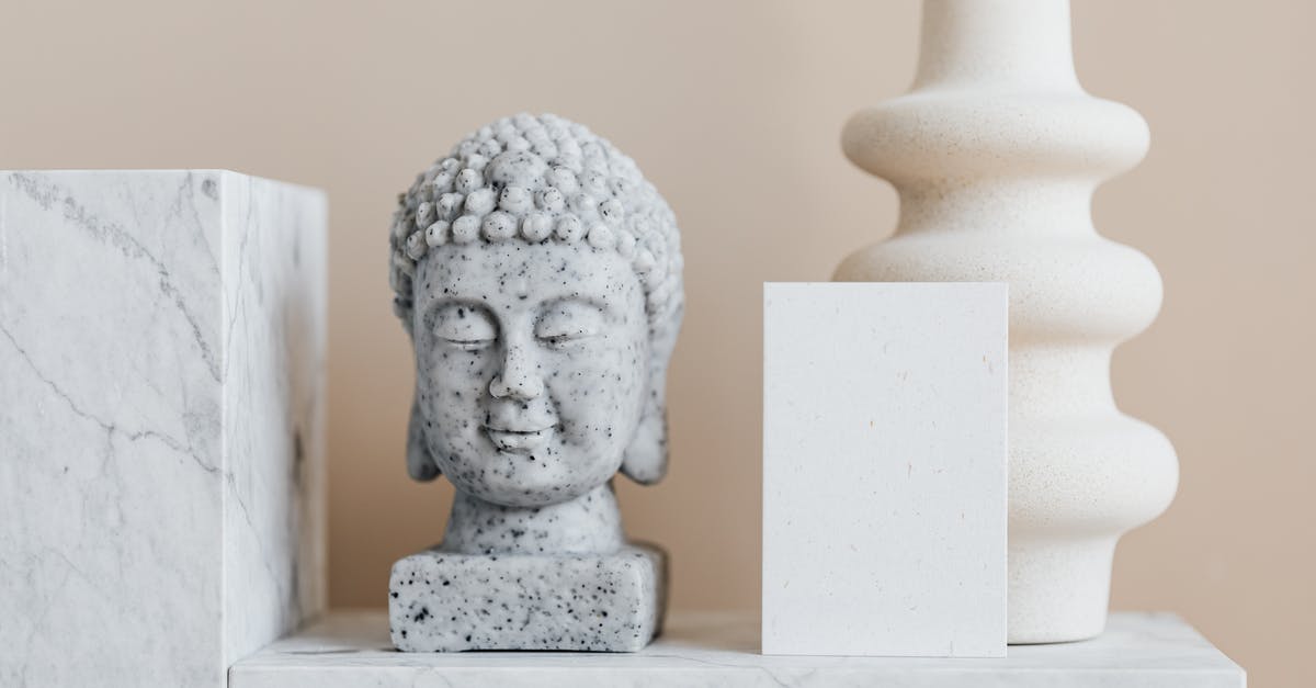 Who wrote the message on the stone? - Granite bust of Buddha placed near white ceramic vase of creative geometric shape and blank card on white marble shelf against beige wall