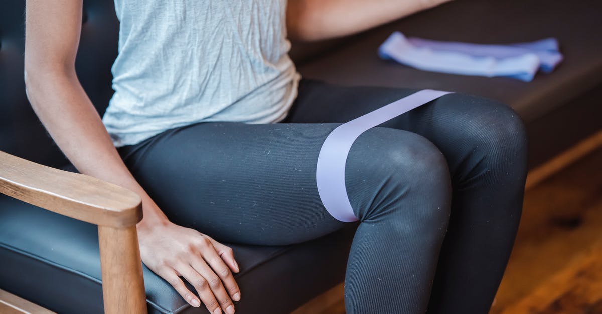 Why are all the Resistance members female? - Faceless slim strong female in sportswear sitting on couch while exercising with elastic resistance band on legs during intense workout