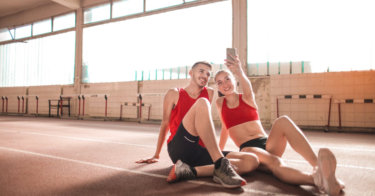 Why can't they track Luther's phone? - Cheerful young sportsmen smiling and taking selfie on smartphone while sitting on floor and resting after training