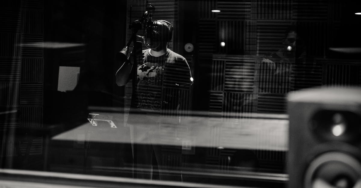 Why Control and his team are singing Russian national anthem? - Through glass of black and white anonymous male musician in headphones singing with microphone while recording song in modern studio