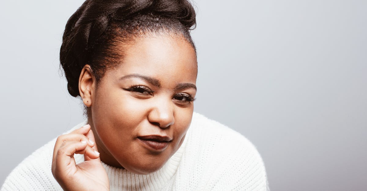 Why did Cass distrust the Doctor? - Positive plus size African American female wearing cozy white knitted sweater standing on gray background in studio and looking at camera with half closed eyes