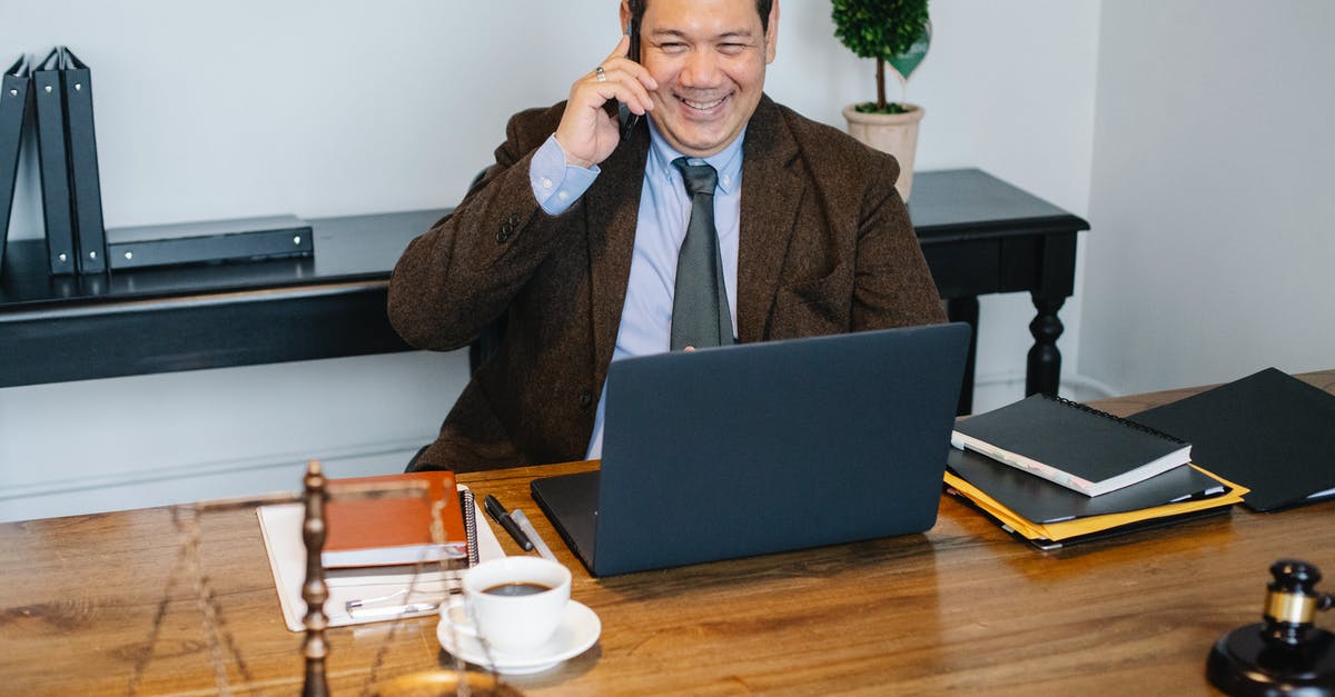 Why did everyone call the organization S.H.I.E.L.D in Captain Marvel? - Joyful Asian male lawyer wearing formal suit having conversation on mobile phone and using laptop while working in modern law firm