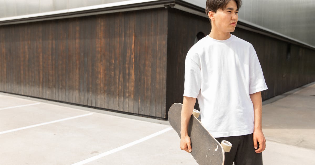 Why did Guy break into Bruno's house? - Handsome young ethnic guy in white t shirt holding skateboard in hand and looking away thoughtfully while resting near modern building after ride