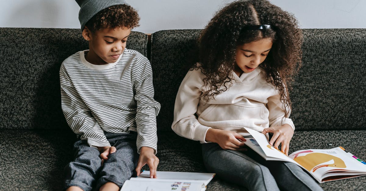 Why did his sister make a scary face? - Grimacing stylish African American siblings reading books and sitting together on cozy couch in living room