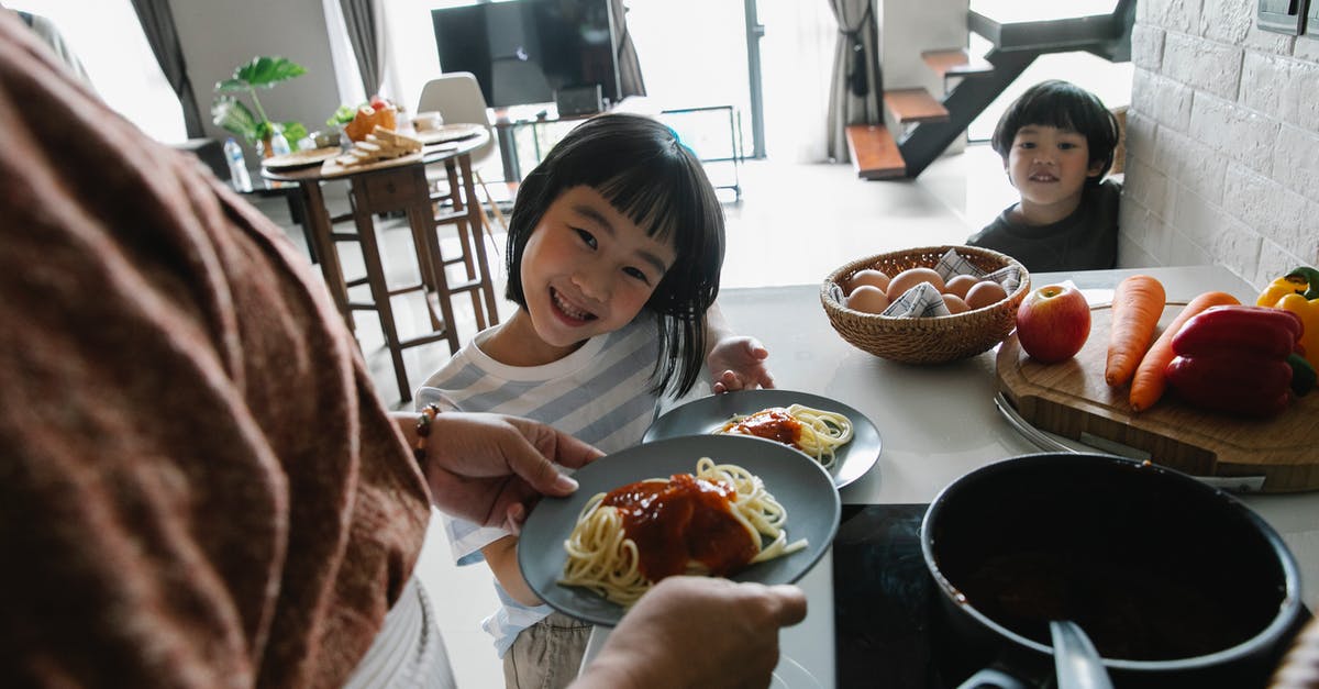 Why did Ilsa Faust wait for high pitch? - High angle of hungry cute little Asian children smiling while waiting for lunch prepared by unrecognizable grandmother standing in kitchen