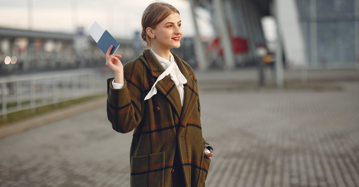 Why did it take the Cops so long to arrive? - Cheerful female passenger wearing trendy plaid coat taking passport and ticket in raised hand while standing on pavement near modern building of airport outside and looking away with smile