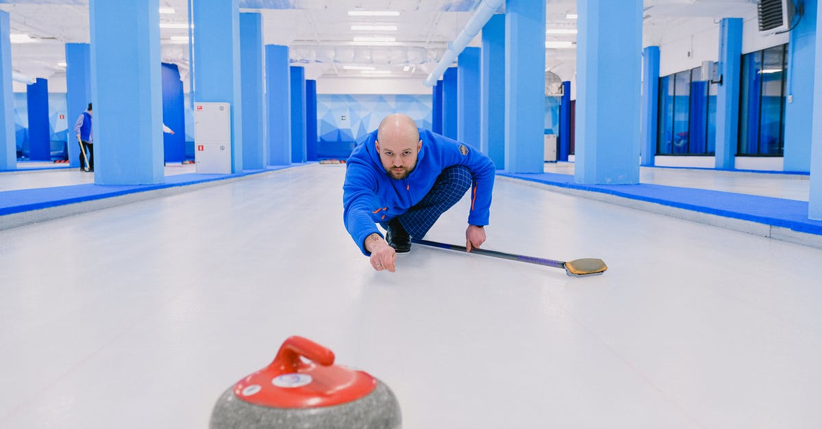Why did Ken steal and then throw away batteries (end of S2E2) - Concentrated sportsman with beard in blue uniform squatting down and looking at sliding stone with red handle during curling game on modern ice rink