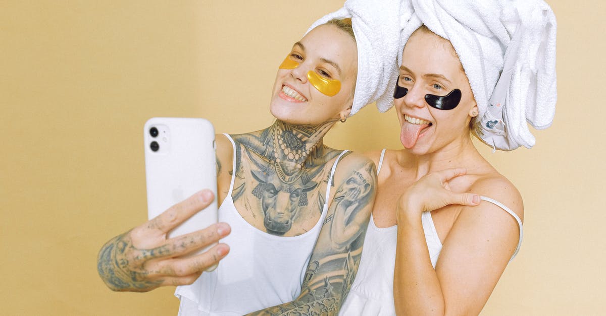 Why did Quint have the tattoo removed? - Optimistic girlfriends in white t shirts with straps bath towels on heads and eye patches standing on beige background and taking selfie on smartphone