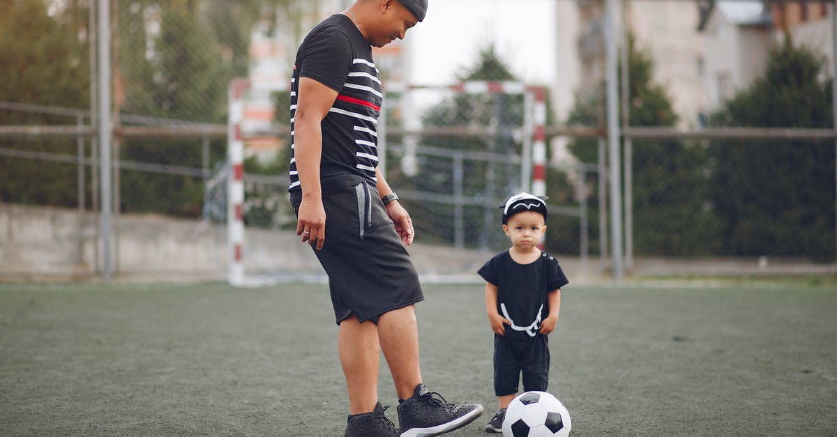 Why did Ricky's dad kick him out? - Full body content ethnic father in black casual clothes with cute toddler son kicking football ball while spending time together on sports ground against football gates