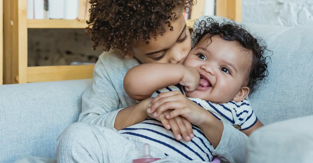 Why did Robert Mariell kiss his sister? - African American boy with curly hair embracing and kissing adorable smiling little baby while sitting in comfortable armchair