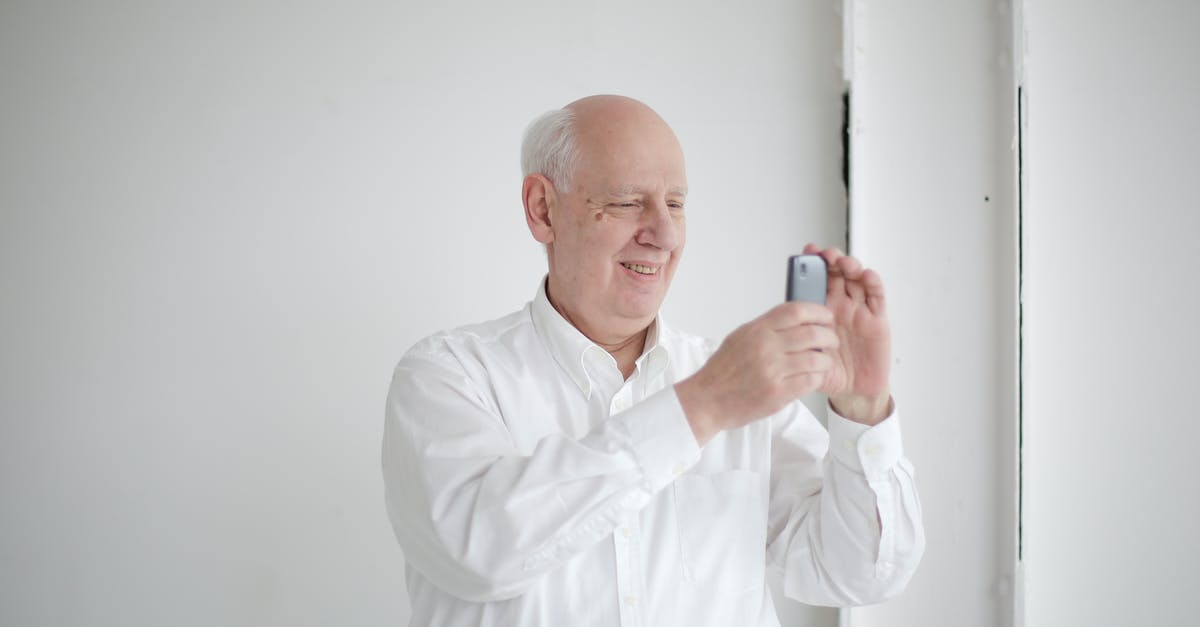 Why did Sebastian Moran shoot the businessman Alfred Meinhard? - Positive old bald man in formal wear taking photo on cellphone while standing against white wall and toothy smiling